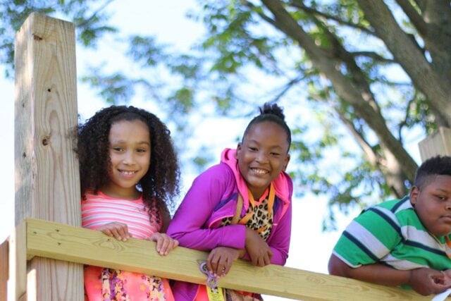 Children standing on playground platform by looking over wooden railing